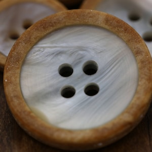 May include: Four brown and white round buttons with four holes each. The buttons have a wood-like rim and a white center with a marbled pattern.