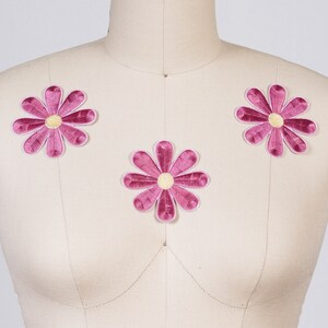 Op de afbeelding: Drie roze viltbloem patches met gele centra. De patches zijn in een driehoekige vorm op een wit mannequin geplaatst.