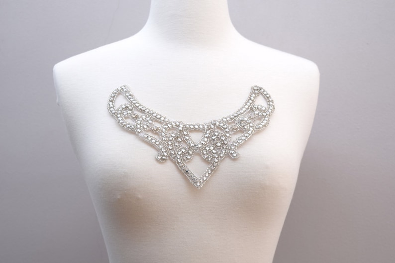 May include: A silver rhinestone embellishment in the shape of a collar. The embellishment is made of small, round rhinestones that are arranged in a delicate, intricate pattern.