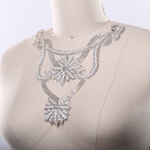 May include: A silver and crystal beaded necklace with a floral design. The necklace is on a white mannequin.