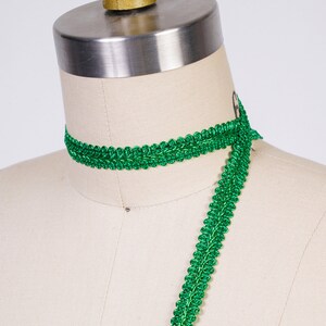 May include: Green braided trim with a shiny finish. The trim is shown wrapped around a dress form.