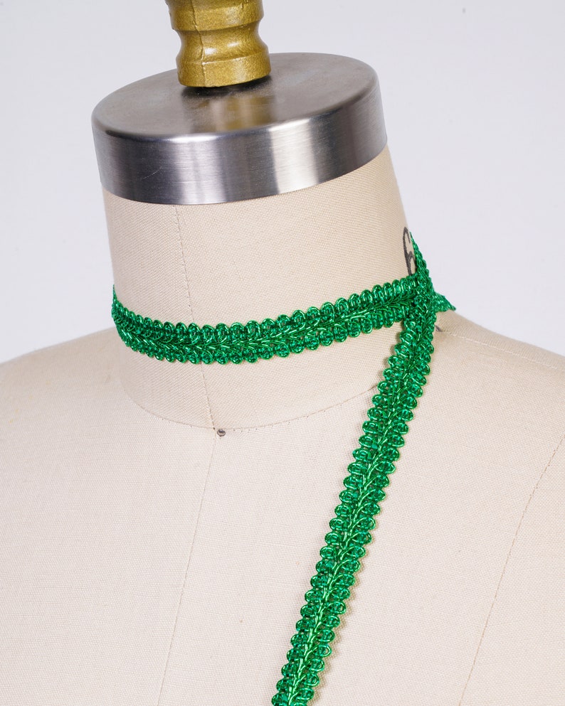 May include: Green braided trim with a shiny finish. The trim is shown wrapped around a dress form.
