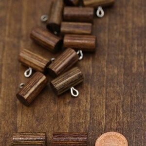 K&ouml;nnte beinhalten: Eine Gruppe von Holz-Toggle-Kn&ouml;pfen mit Metallschlaufen. Die Kn&ouml;pfe sind braun mit dunkelbraunen Streifen. Zwei Kn&ouml;pfe sind im Vordergrund, mit einer Penny-M&uuml;nze im Hintergrund.