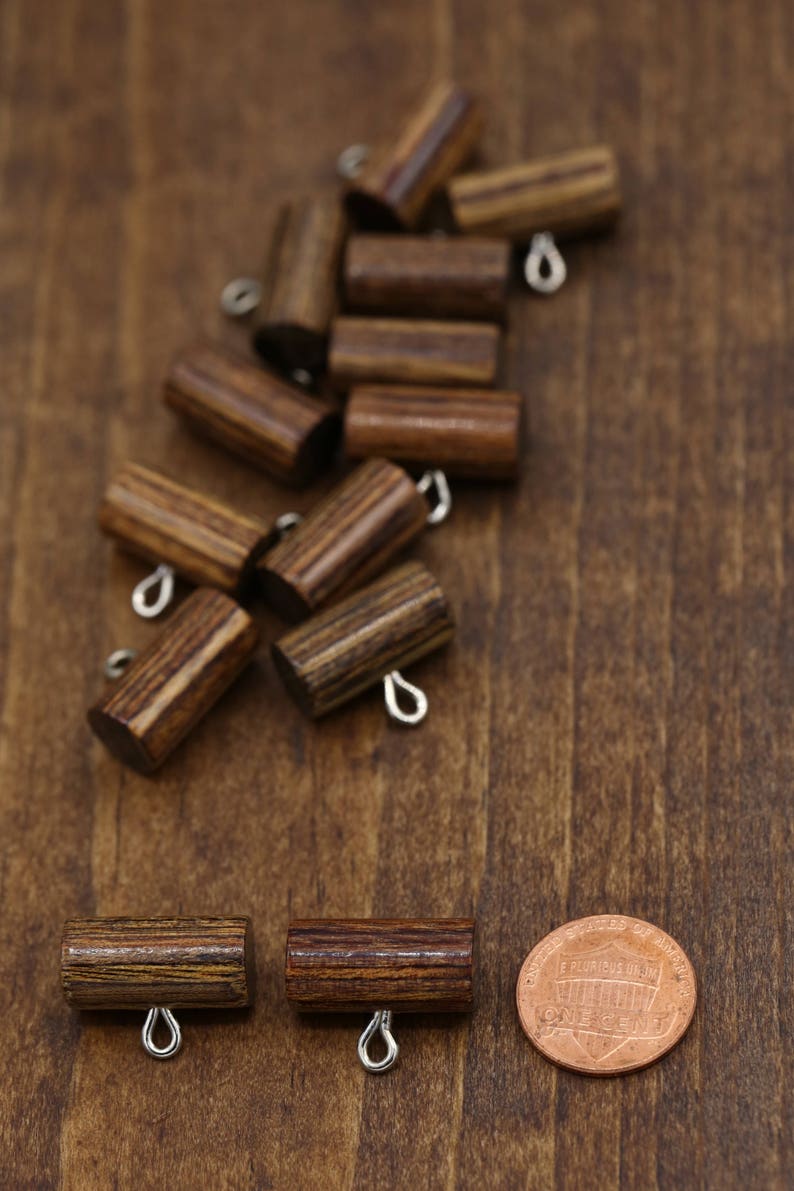 K&ouml;nnte beinhalten: Eine Gruppe von Holz-Toggle-Kn&ouml;pfen mit Metallschlaufen. Die Kn&ouml;pfe sind braun mit dunkelbraunen Streifen. Zwei Kn&ouml;pfe sind im Vordergrund, mit einer Penny-M&uuml;nze im Hintergrund.
