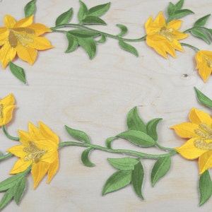 Pode incluir: Apliques de flores amarelas bordadas com folhas verdes dispostas em um padrão circular sobre um fundo de madeira claro.