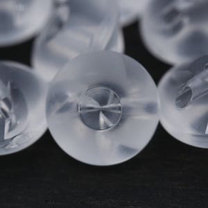 Puede incluir: Primer plano de cuentas de plástico transparente con un diseño en relieve. Las cuentas son redondas y tienen una superficie lisa.