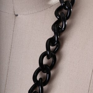 May include: A close-up of a black chain made of thick, chunky links. The chain is made of a smooth, glossy material.