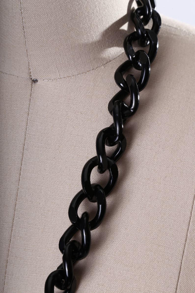 May include: A close-up of a black chain made of thick, chunky links. The chain is made of a smooth, glossy material.