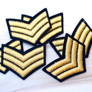 May include: A set of six black and gold chevron patches. The patches are made of fabric and have a stitched design.