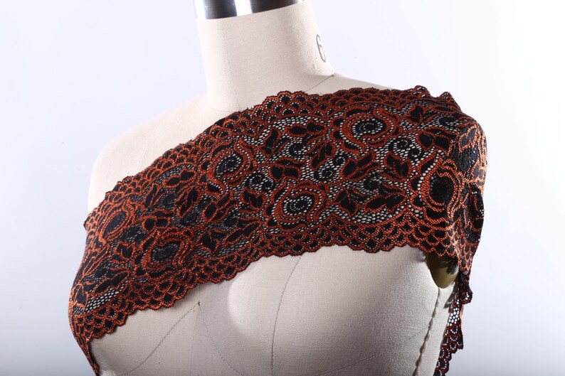 May include: Black and orange lace trim with a floral pattern. The lace is delicate and intricate, with a scalloped edge.