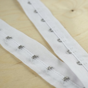May include: White fabric with metal hooks and eyes for sewing on clothing.