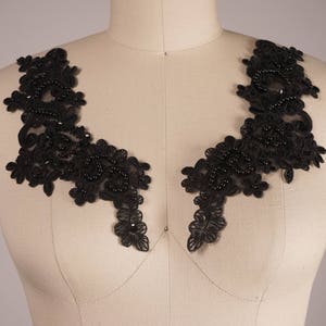 May include: Two black lace appliques with beaded embellishments. The appliques are shaped like a V and are perfect for adding a touch of elegance to any garment.