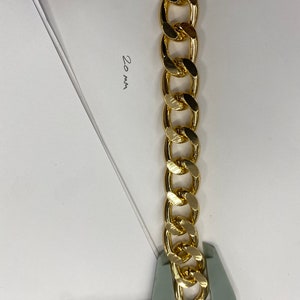 May include: A gold chain link measuring 20 mm in width. The chain is being measured with a ruler.