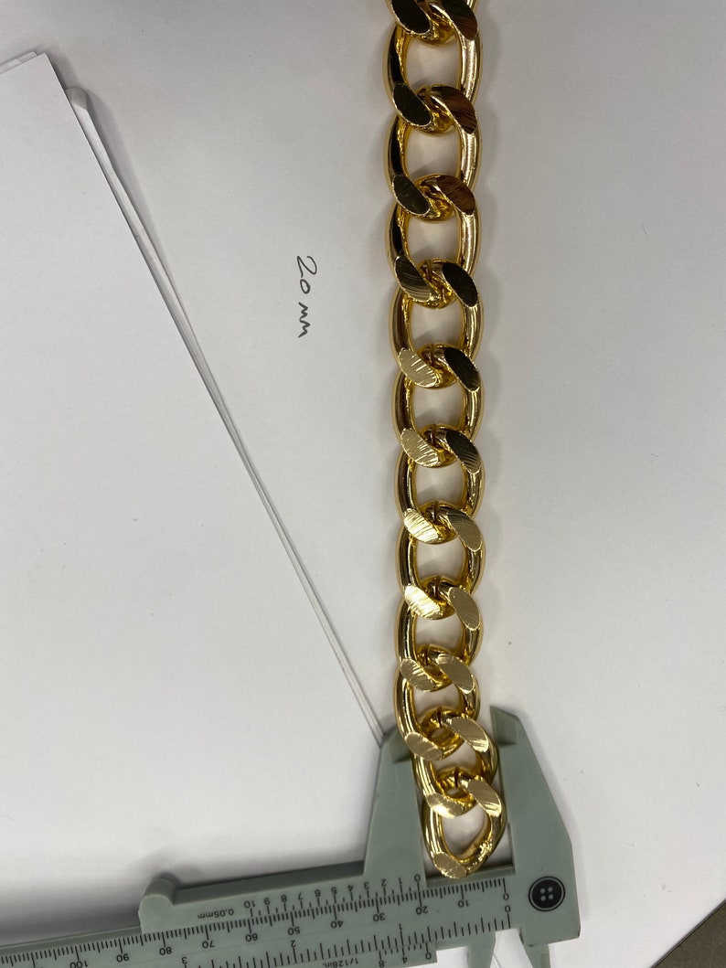May include: A gold chain link measuring 20 mm in width. The chain is being measured with a ruler.