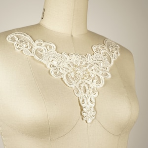 May include: A delicate white lace applique with a floral design. The lace is beaded and has a scalloped edge.