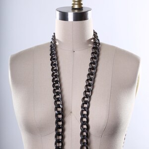 May include: A black chain necklace on a white dress form with a gold top.