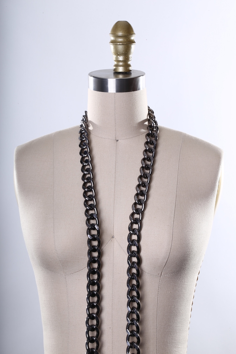 May include: A black chain necklace on a white dress form with a gold top.