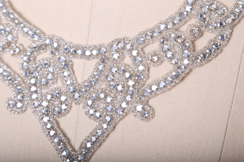 May include: A silver beaded embellishment with a delicate floral design. The embellishment is perfect for adding a touch of sparkle to clothing, accessories, or home decor.