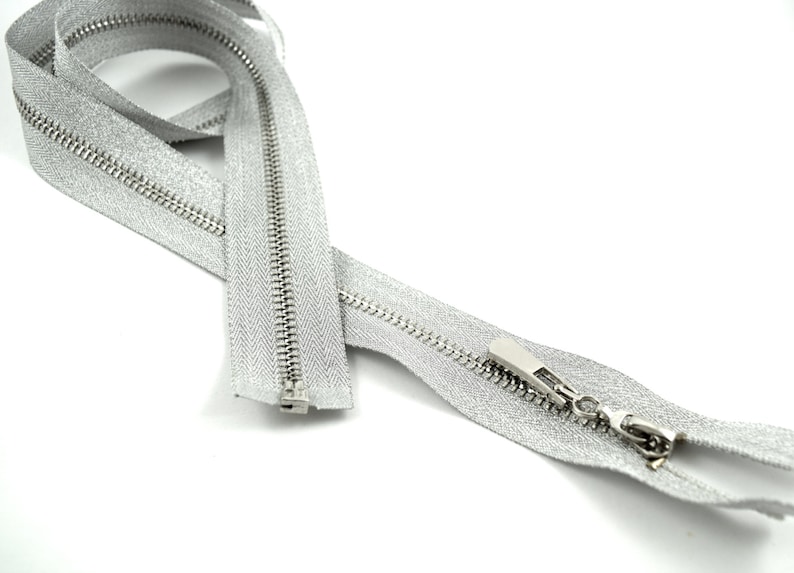 May include: A silver zipper with a silver slider. The zipper is closed and lying on a white surface.