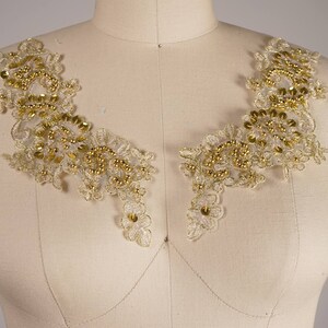 Puede incluir: Un par de apliques de encaje dorado con detalles de cuentas. Los apliques tienen forma de V y son perfectos para agregar un toque de elegancia a cualquier prenda.
