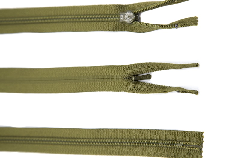 May include: Three olive green zippers with metal sliders. The zippers are open and the slider is in the middle of the zipper.