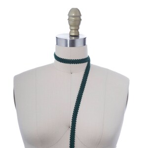 May include: A dark green trim with a decorative pattern is draped over a white dress form.