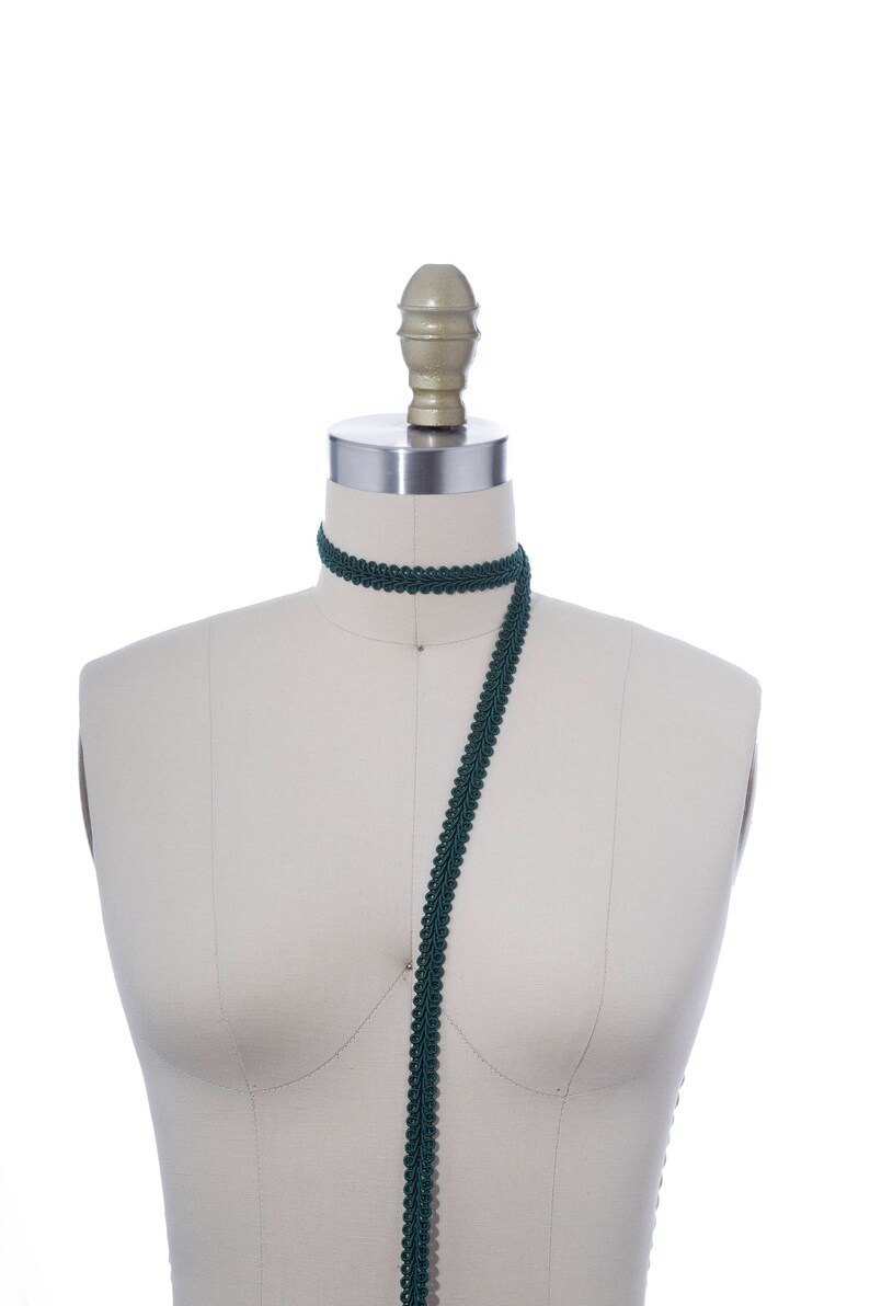 May include: A dark green trim with a decorative pattern is draped over a white dress form.