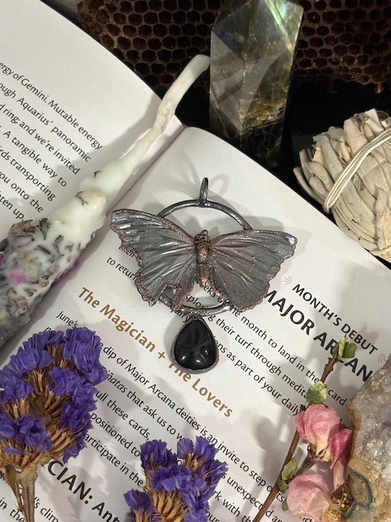 A real butterfly wing encased in electroformed copper alongside a black onyx teardrop — wearable nature meets gothic alchemy, no two are identical.