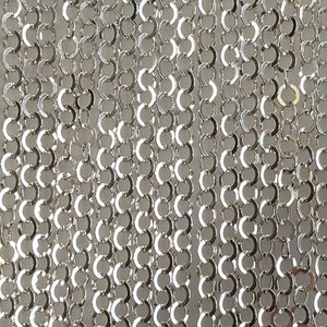 May include: A close-up of a silver chain made of small, interconnected rings. The chain is smooth and shiny, with a metallic finish.