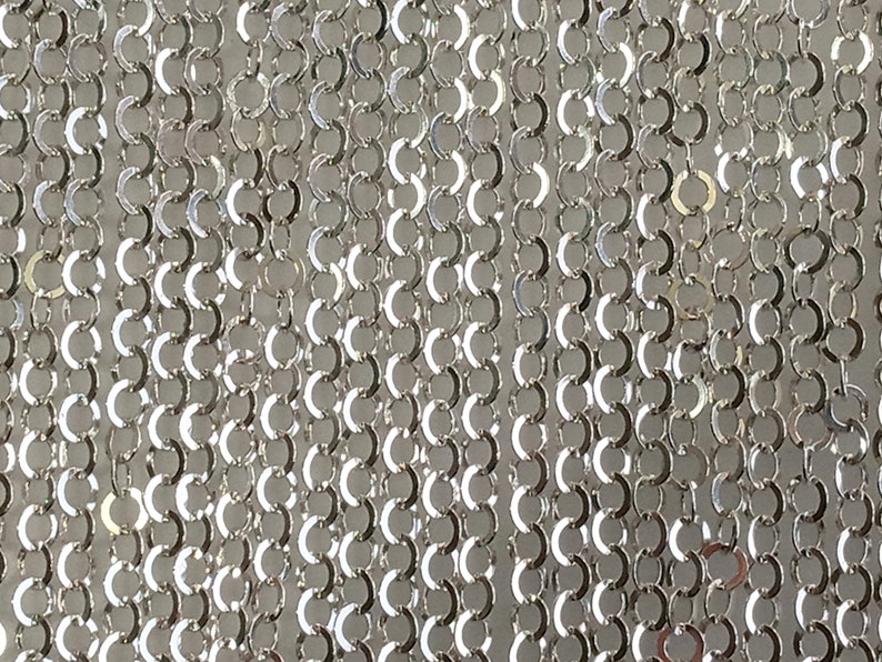 May include: A close-up of a silver chain made of small, interconnected rings. The chain is smooth and shiny, with a metallic finish.