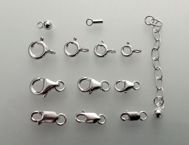 May include: A collection of silver-toned jewelry findings, including jump rings, lobster clasps, and a small chain.
