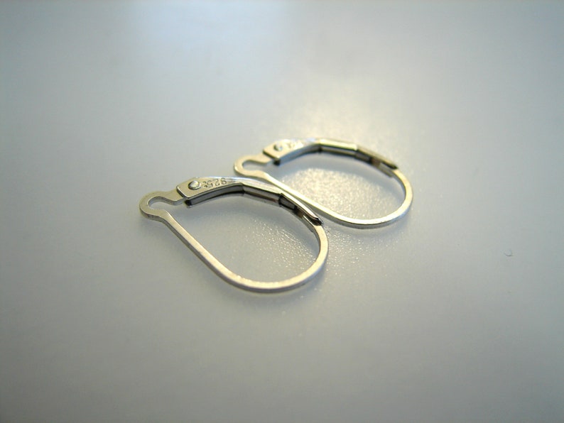 May include: A pair of silver earring hooks with a small, clear, round stone on each hook. The hooks are marked with the number "2025".