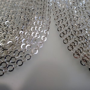 May include: A close-up of a silver chain, made of small, linked oval shapes. The chain is folded in half, with the two halves overlapping.