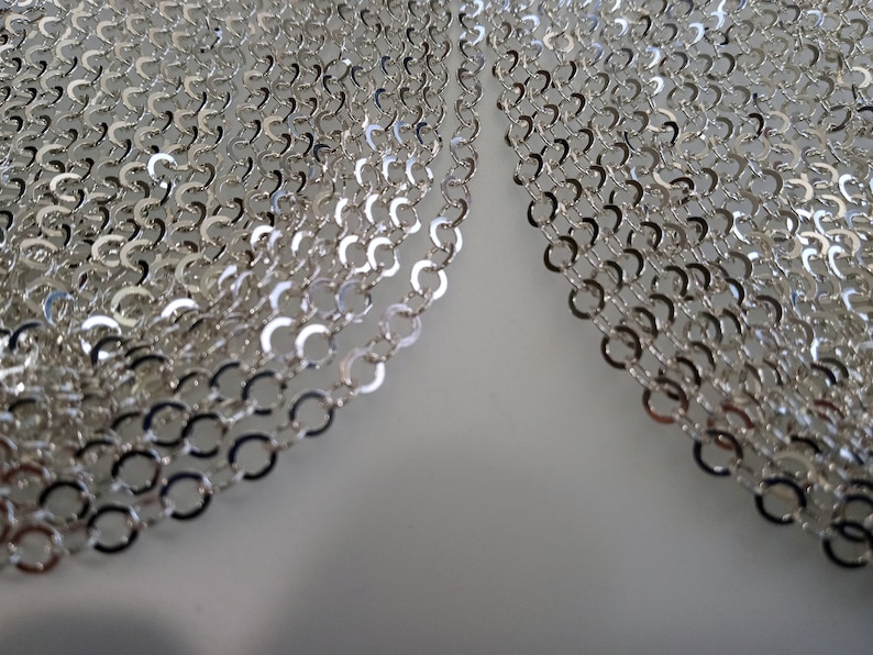 May include: A close-up of a silver chain, made of small, linked oval shapes. The chain is folded in half, with the two halves overlapping.