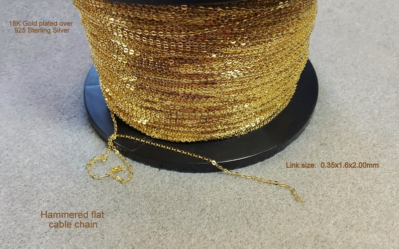 K&ouml;nnte beinhalten: Eine Spule mit goldbeschichteter, gehammerter, flacher Kabelkette aus 925er Sterlingsilber. Die Kette ist auf einer schwarzen Spule aufgerollt. Die Gliedergr&ouml;&szlig;e betr&auml;gt 0,35x1,6x2,00mm.