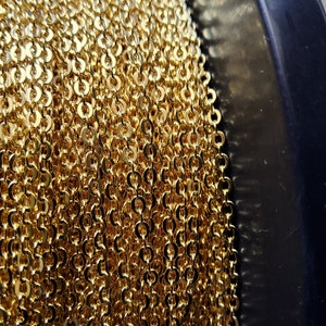 K&ouml;nnte beinhalten: Nahaufnahme einer Spule mit goldfarbener Kette. Die Kette besteht aus kleinen, kreisf&ouml;rmigen Gliedern, die eng aneinander gewickelt sind. Die Kette hat eine helle, gl&auml;nzende Goldfarbe, und die Spule ist schwarz.