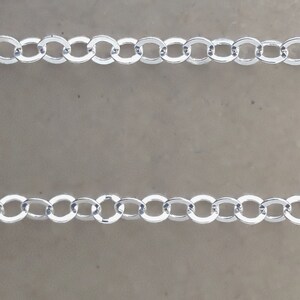 May include: Two rows of silver chain links on a light brown background.