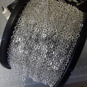 May include: A spool of silver chain, wound tightly and ready to be used for jewelry making or other craft projects.
