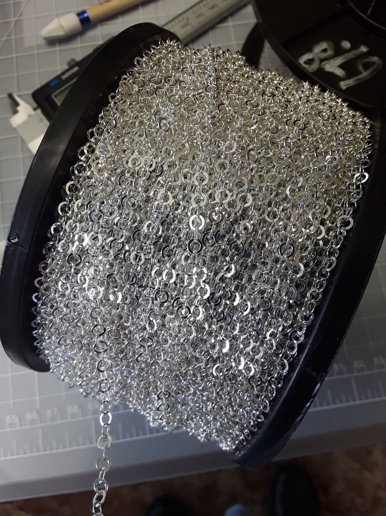 May include: A spool of silver chain, wound tightly and ready to be used for jewelry making or other craft projects.