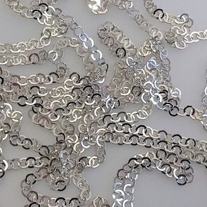 May include: A silver chain made of interlocking oval links. The chain is lying on a white surface.