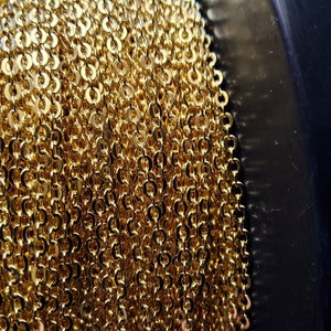 K&ouml;nnte beinhalten: Nahaufnahme einer Spule mit goldfarbener Kette. Die Kette besteht aus kleinen, miteinander verbundenen kreisf&ouml;rmigen Gliedern, die eine dichte, strukturierte Oberfl&auml;che bilden. Die Kette ist um eine schwarze Spule gewickelt.