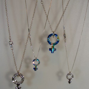 May include: Four silver necklaces with different blue and green crystal pendants in the shape of a female symbol.