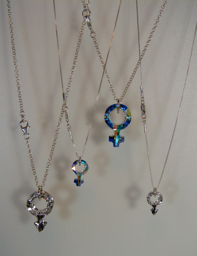 May include: Four silver necklaces with different blue and green crystal pendants in the shape of a female symbol.