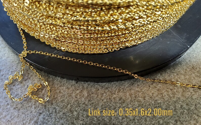 K&ouml;nnte beinhalten: Eine Spule goldfarbener Kette mit einem filigranen, verbundenen Design. Die Kette ist auf einer schwarzen Oberfl&auml;che aufgerollt. Der Text "Link size: 0.35x1.6x2.00mm" ist sichtbar.