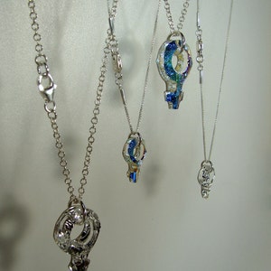 May include: Four silver necklaces with different length chains and key-shaped pendants. The pendants are made of iridescent glass with blue, green, and yellow hues.