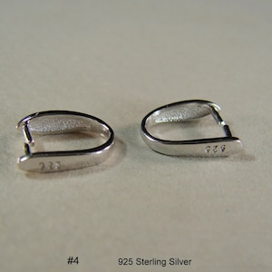 May include: Two silver 925 sterling silver crimp beads, each with a small opening on one side. The beads are designed to be used for jewelry making.