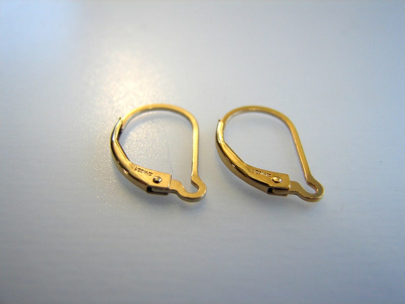 May include: A pair of gold-toned earring hooks. The hooks are made of metal and have a spring-loaded closure. The hooks are approximately 2.5 cm long.
