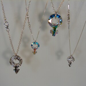 May include: Four silver necklaces with different pendants. Each pendant is a silver symbol of the female gender, with a different iridescent crystal design.