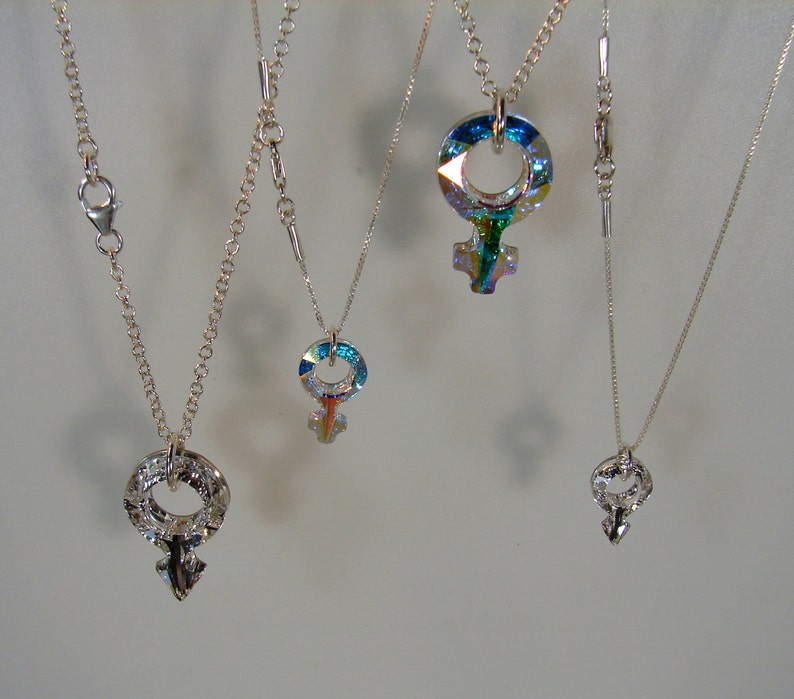 May include: Four silver necklaces with different pendants. Each pendant is a silver symbol of the female gender, with a different iridescent crystal design.