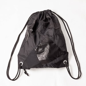May include: A black drawstring bag made from a patchwork of different fabrics. The bag has a cinched top and two long drawstrings.